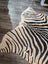 A large cowhide plush zebra print rug with bold black and tan stripes on cream base by angus oliver