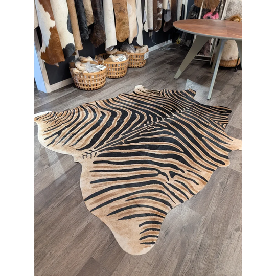 Large cowhide zebra printed rug with bold black and tan stripes on wooden floor by angus oliver