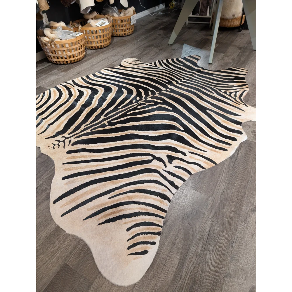 A large cowhide zebra print faux leather rug with bold black and beige stripes by angus oliver showcasing unique characteristics on wood floor