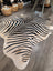 A large cowhide zebra print faux leather rug with bold black and beige stripes by angus oliver showcasing unique characteristics on wood floor