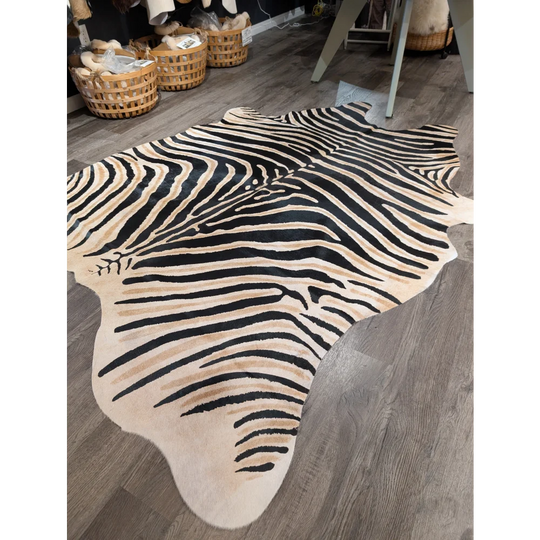 A large cowhide zebra print faux leather rug with bold black and beige stripes by angus oliver showcasing unique characteristics on wood floor