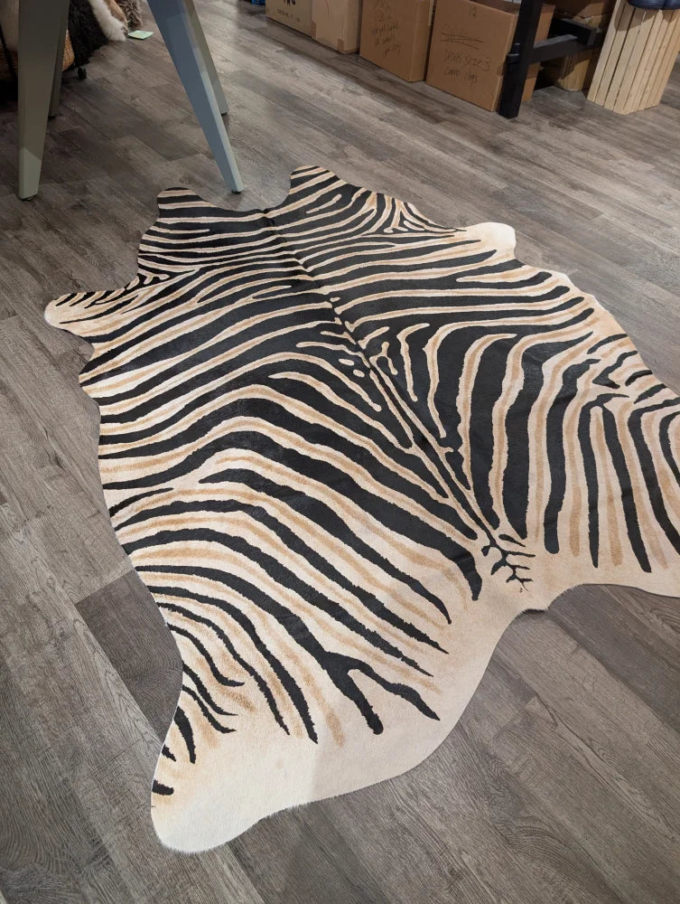 A large cowhide faux leather rug with bold zebra print in black and beige on gray wood floor by angus oliver