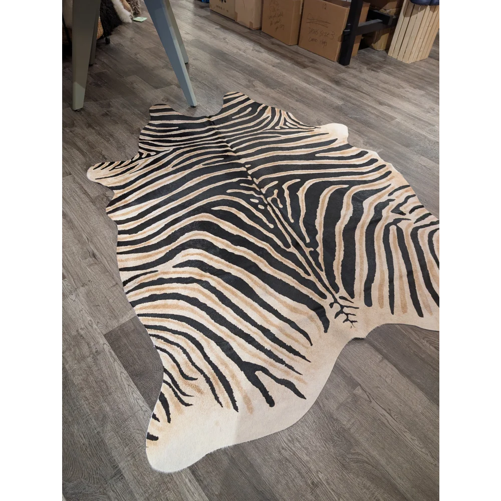 A large cowhide faux leather rug with bold zebra print in black and beige on gray wood floor by angus oliver