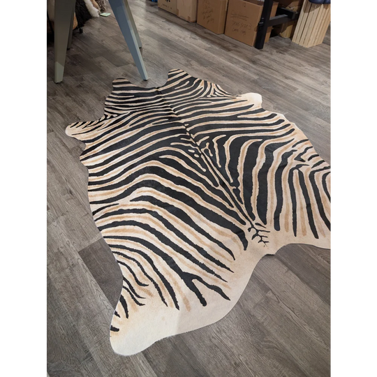 A large cowhide faux leather rug with bold zebra print in black and beige on gray wood floor by angus oliver